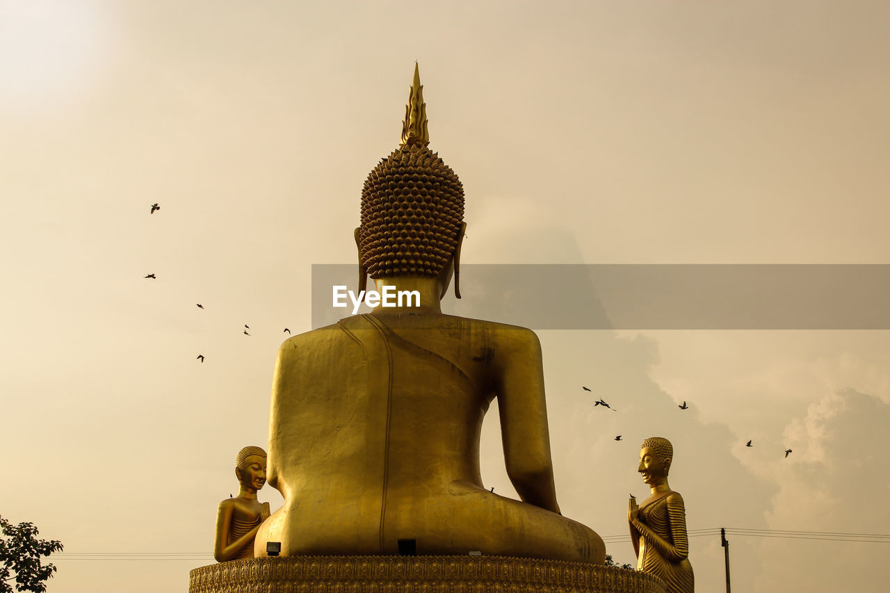 Low angle view of golden buddha statue against sky on sunny day