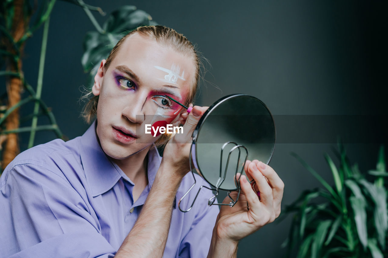 Man applying make-up on face looking in hand mirror