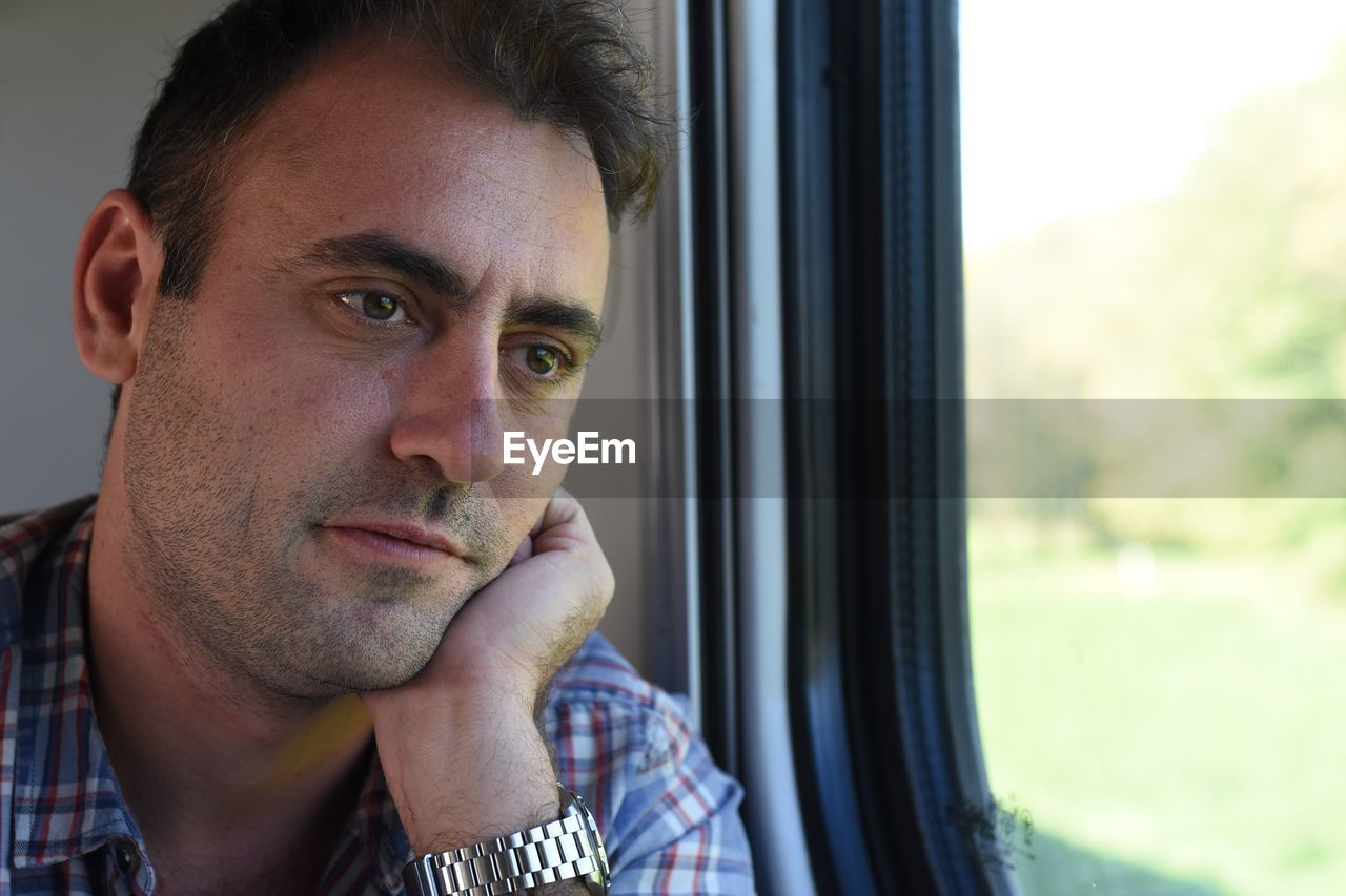 Close-up of thoughtful mid adult man looking through window in train