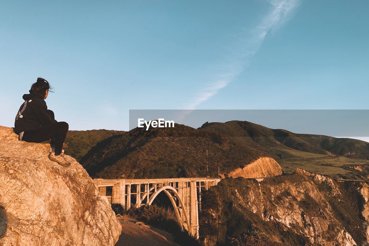 Woman on bridge by mountains against sky