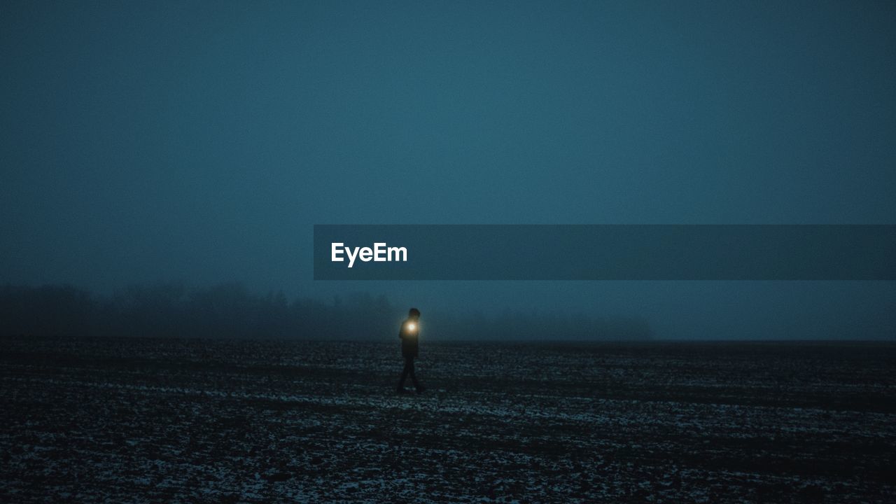 Man with flashlight walking on land against sky at night