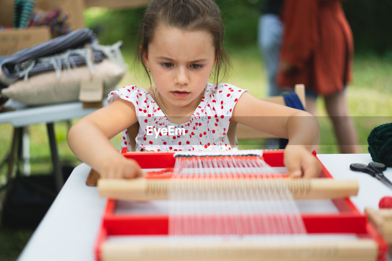 Girl weaving small rug with pattern at masterclass on weaving.