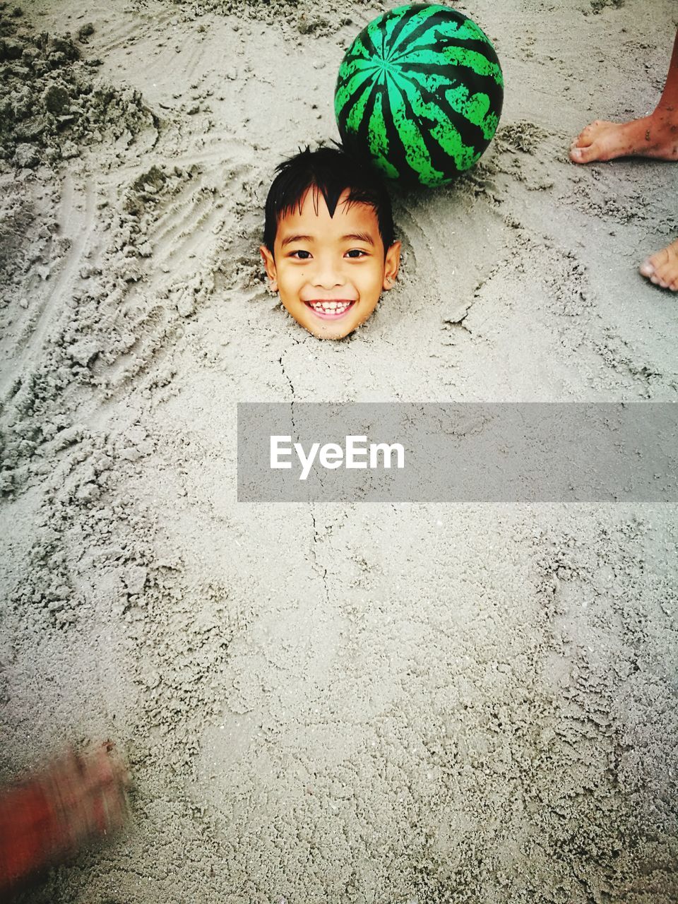 High angle portrait of playful boy buried in sand at beach