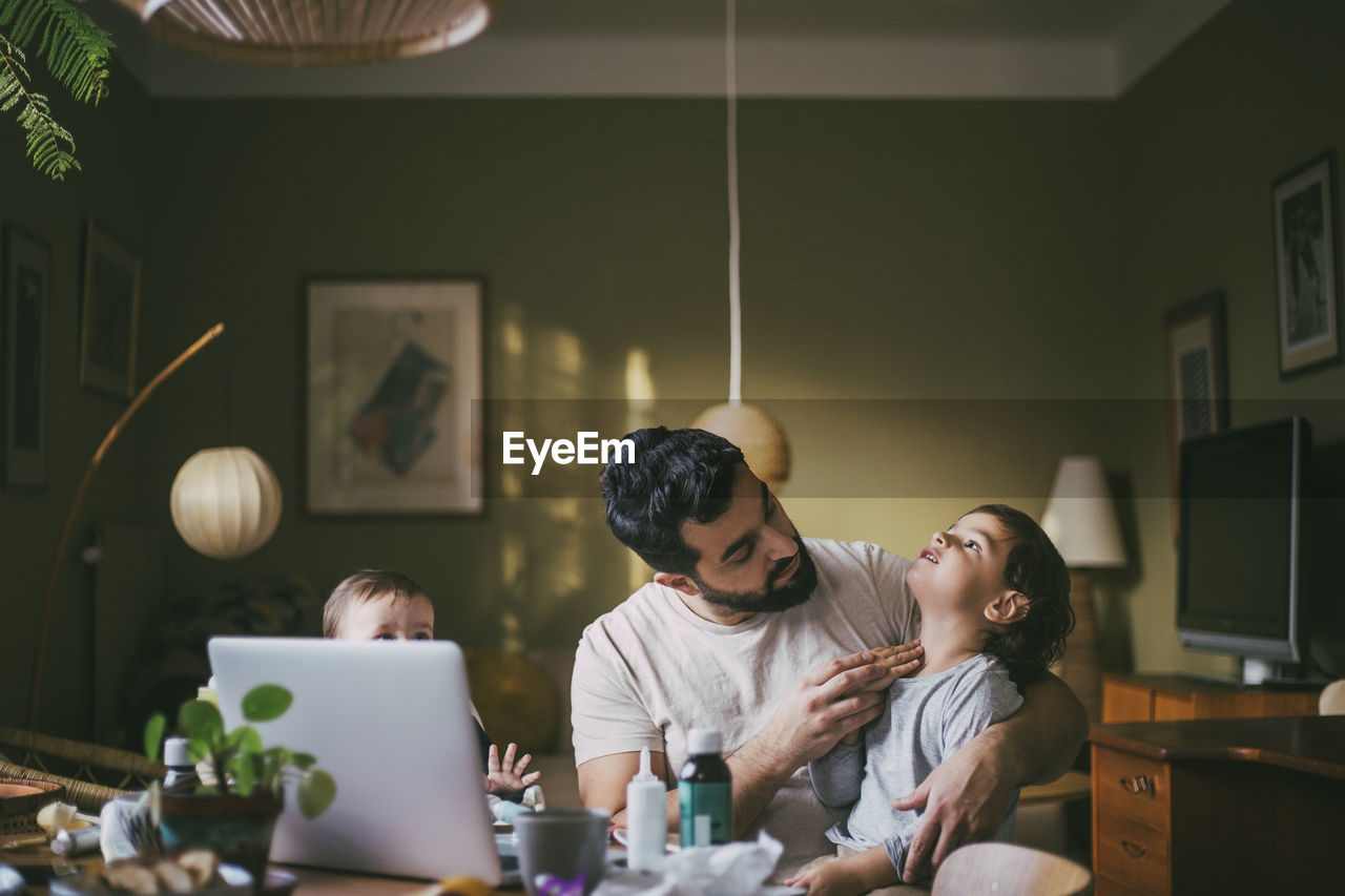 Father with children taking advice on video call through laptop at home during covid-19