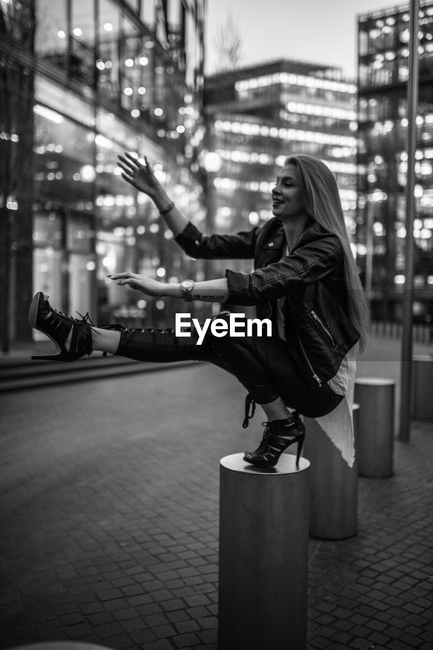 Young woman crouching on bollard in city at night