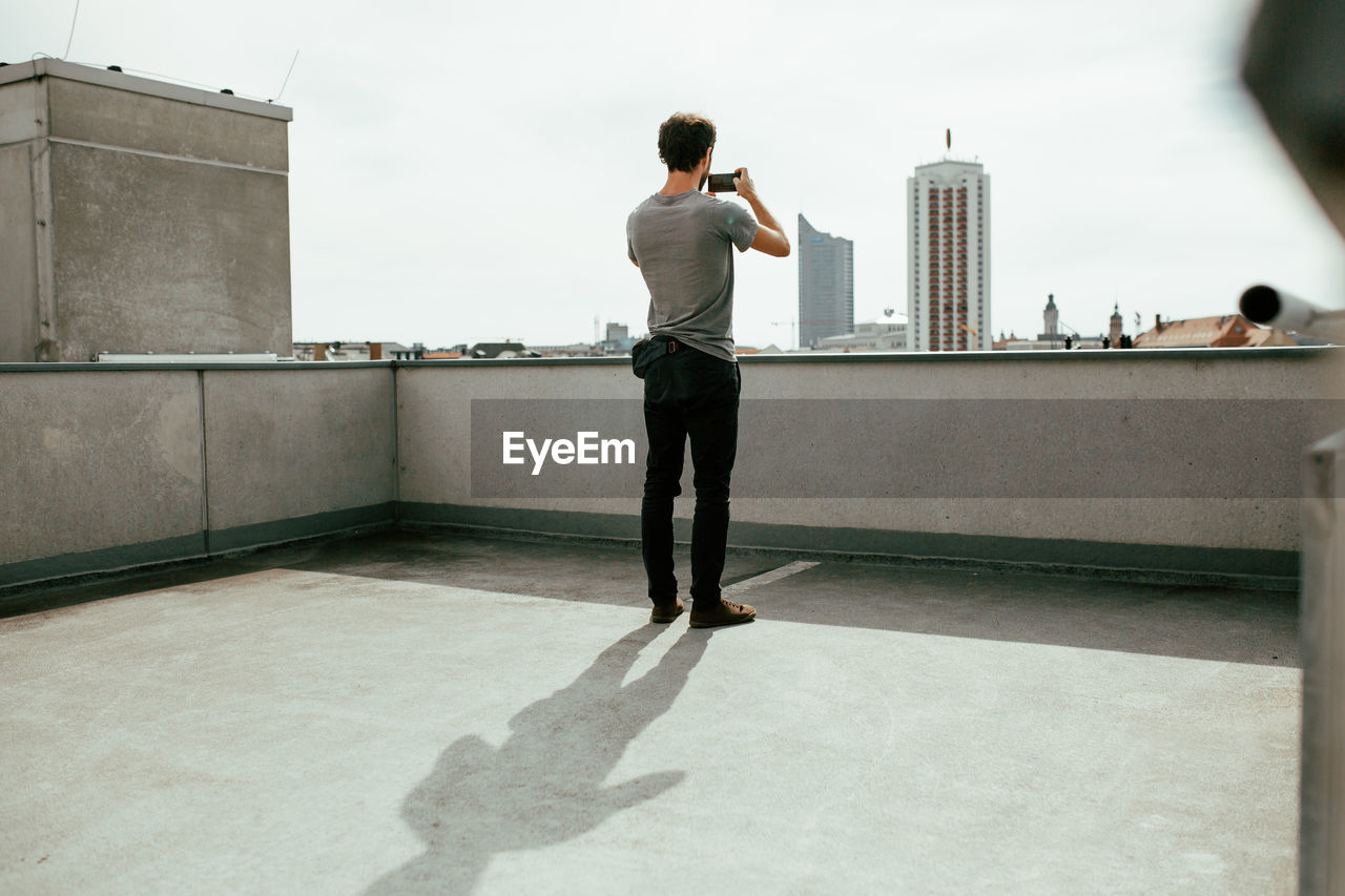 Rear view of man photographing on building terrace during sunny day