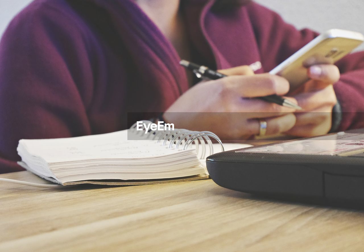 Midsection of woman using phone at table