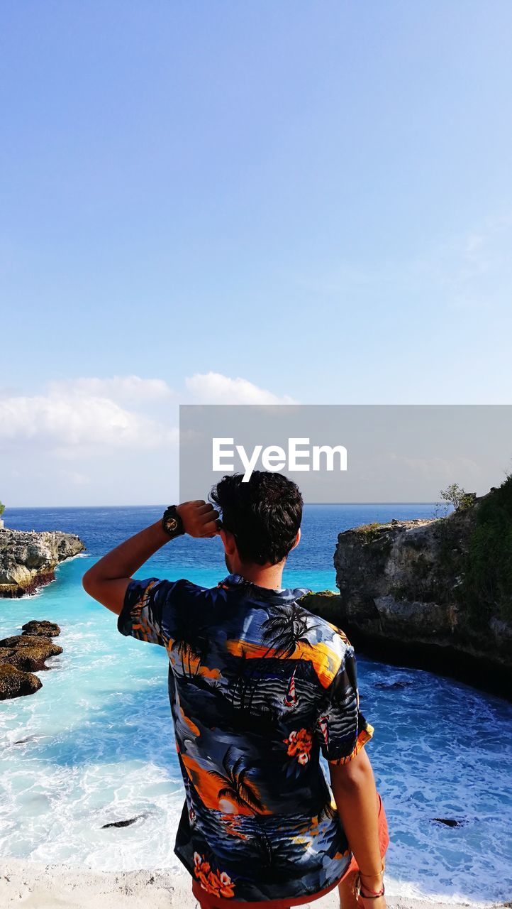 Rear view of man standing at beach against sky