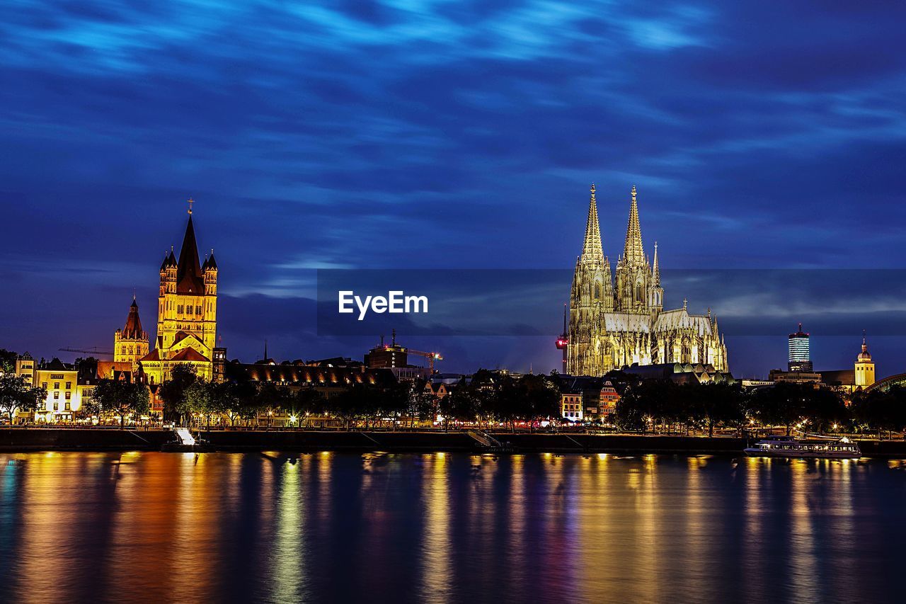 ILLUMINATED BUILDING BY RIVER AGAINST SKY