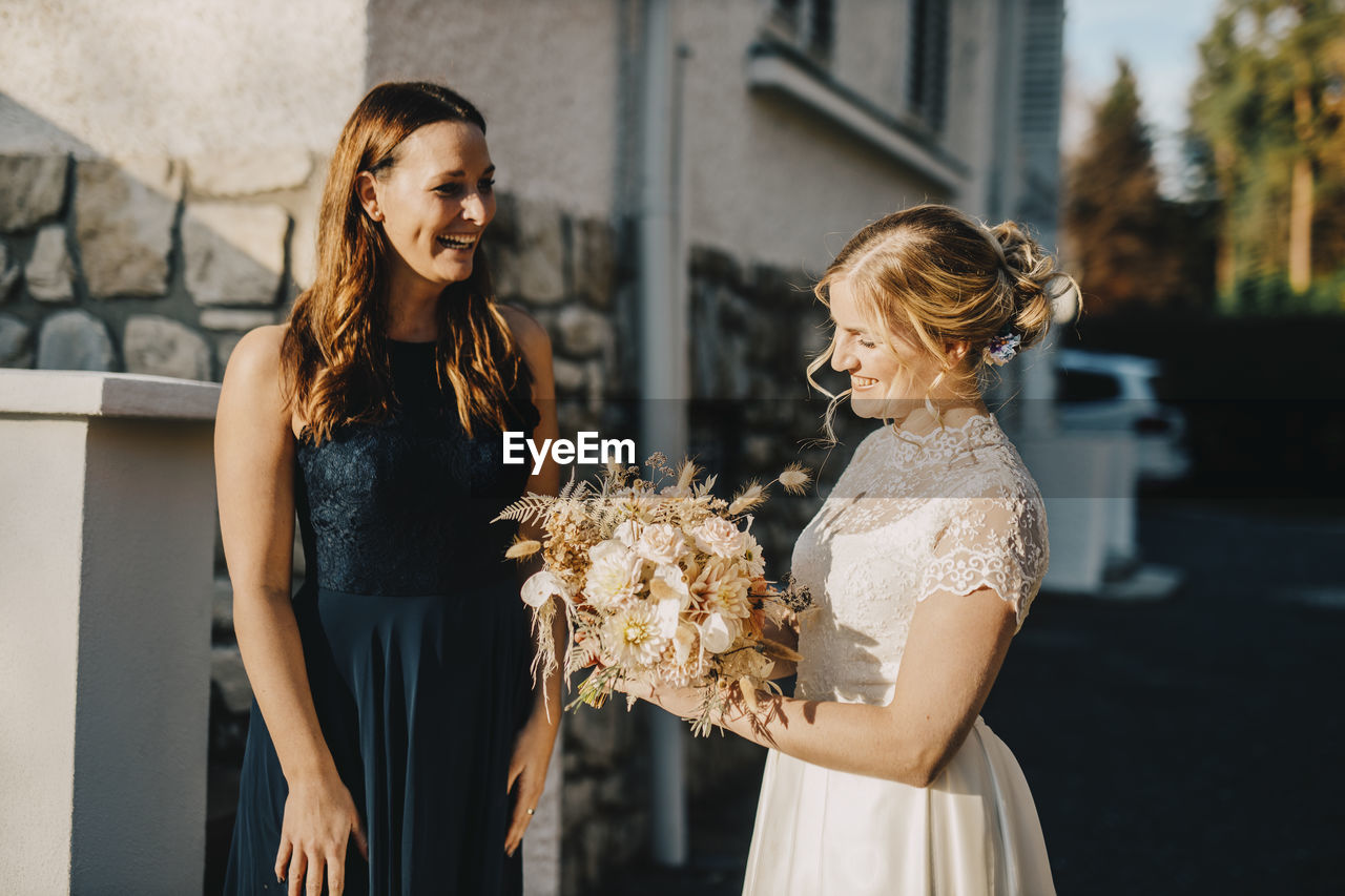 Bride holding bouquet while standing with friend during wedding ceremony