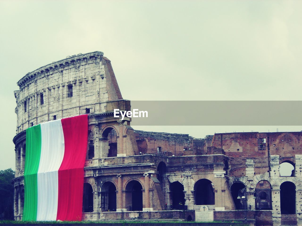 Low angle view of historic coliseum with italian flag against sky