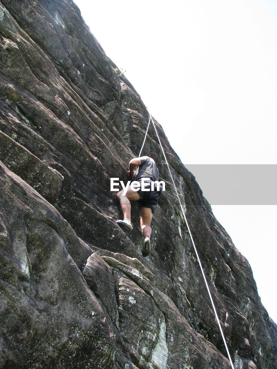 Low angle view of man climbing rock against clear sky