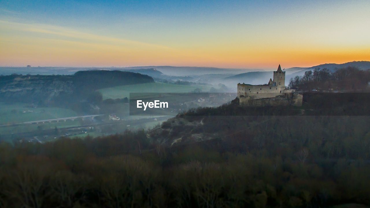SCENIC VIEW OF BUILDING BY MOUNTAINS AGAINST SKY DURING SUNSET