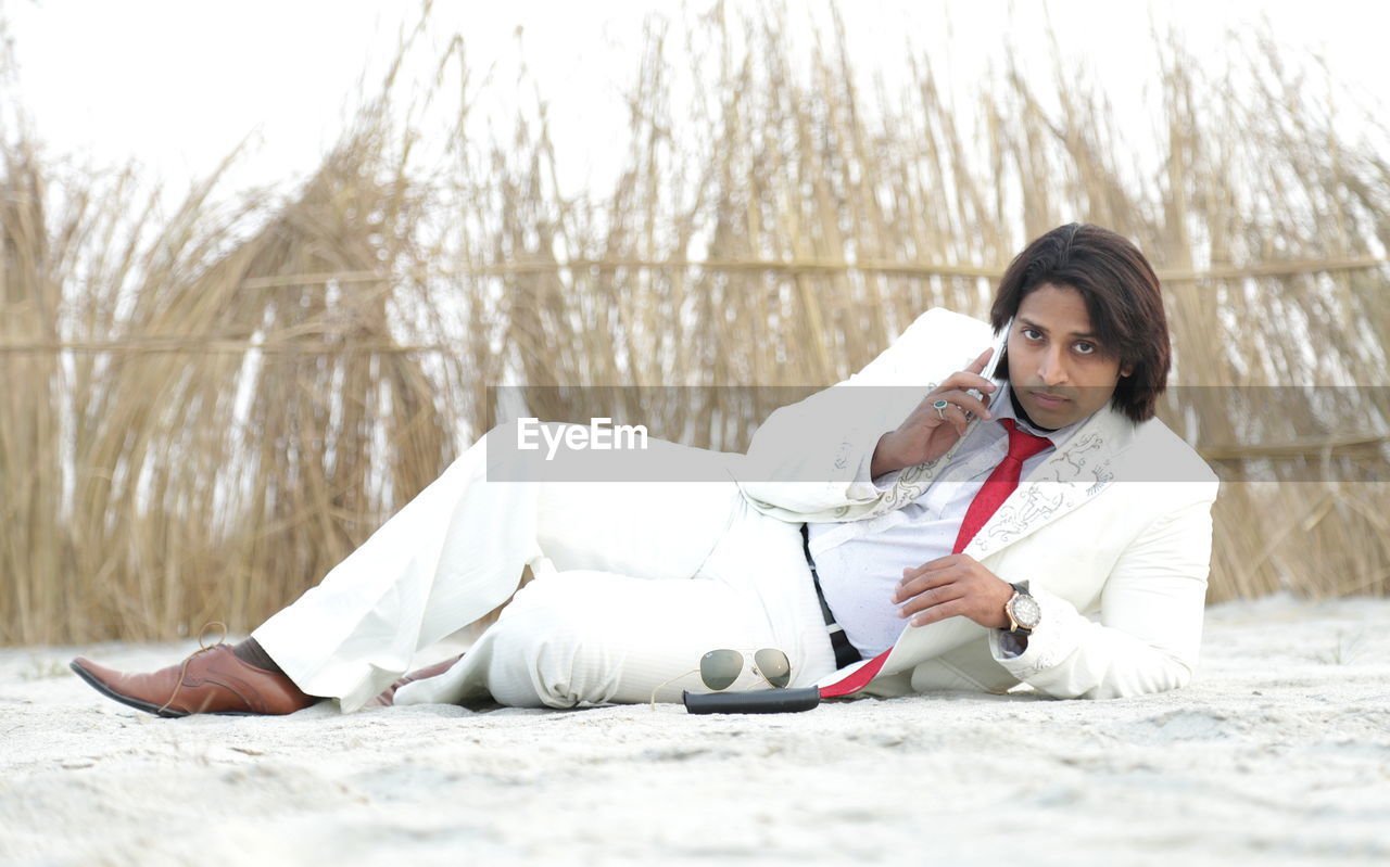 Man in white suit using phone on beach