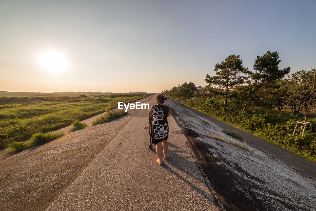 REAR VIEW OF WOMAN WALKING ON ROAD BY PLANTS