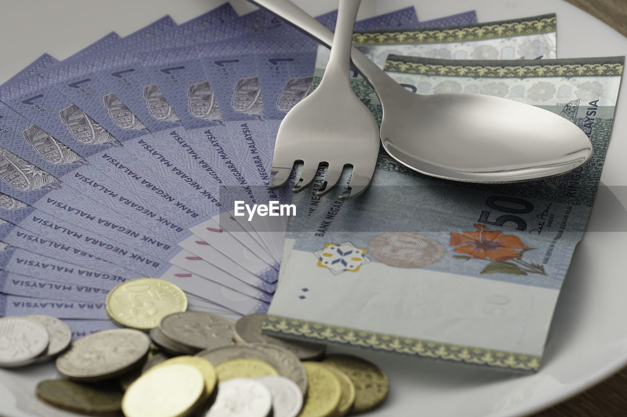 High angle view of paper currencies with coins and cutleries in plate