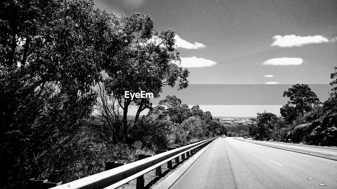 Empty road by trees against sky