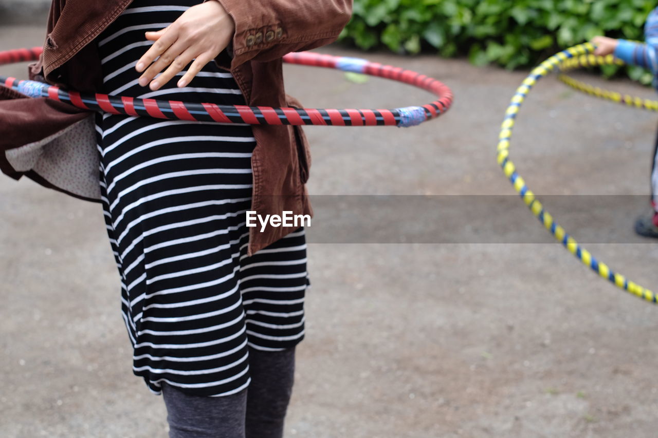 Midsection of woman with hula hoop standing on footpath