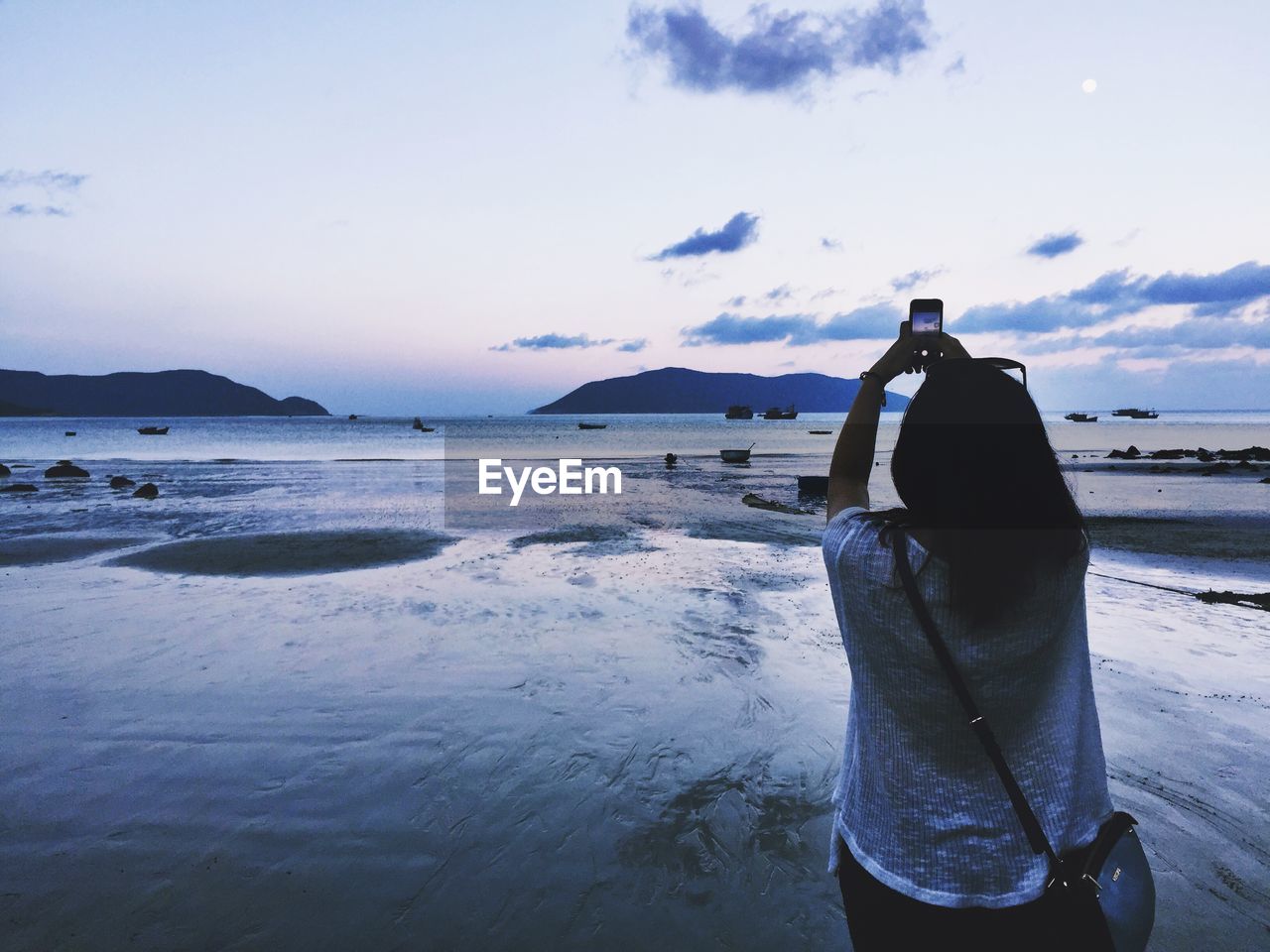 Rear view of woman photographing sky at beach during sunset