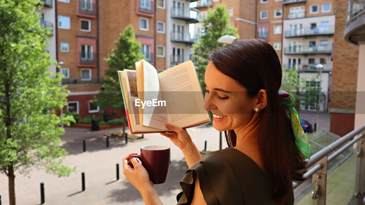 Smiling young woman holding coffee cup and book