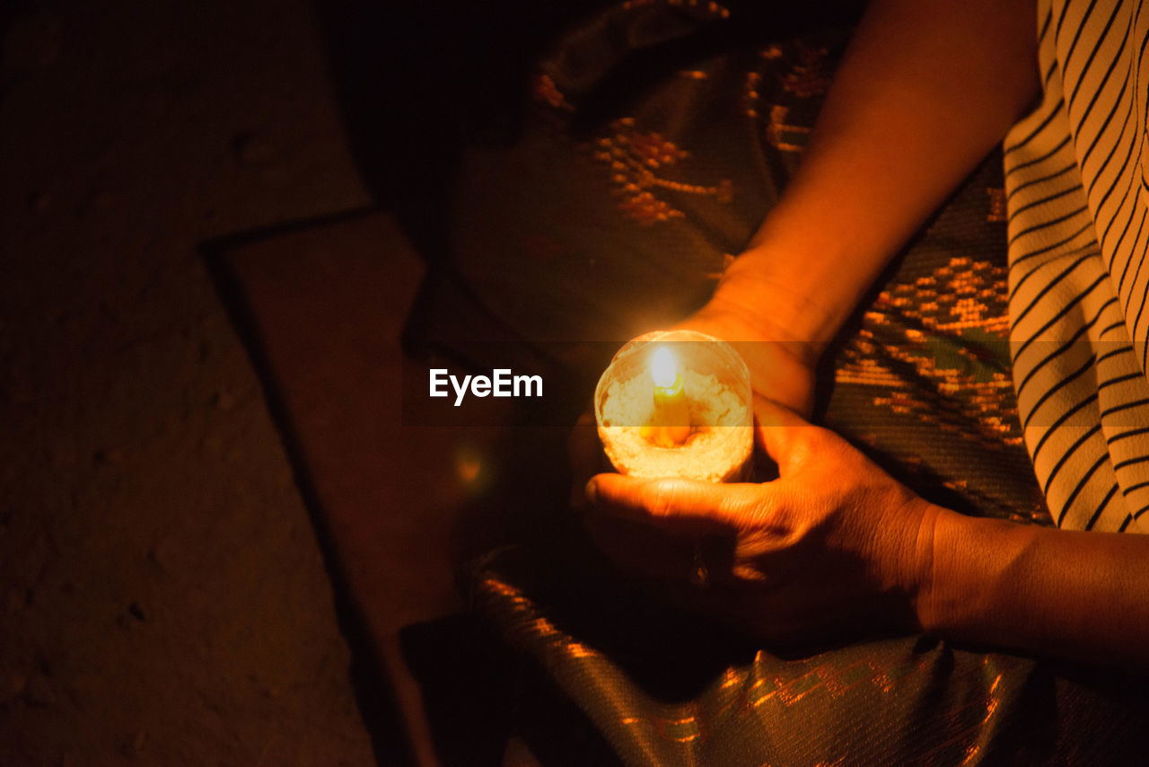 Midsection of woman holding illuminated candle while praying on floor