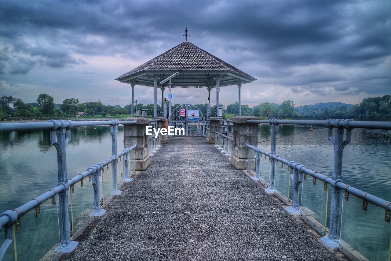 Empty gazebo over river against cloudy sky
