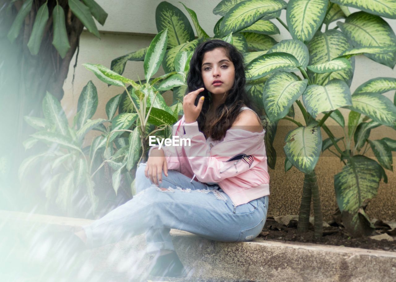 Portrait of a young woman sitting against plants