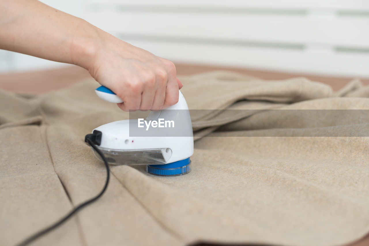 Woman uses a machine for removing pellet and spools from clothes and fabric on black trousers.