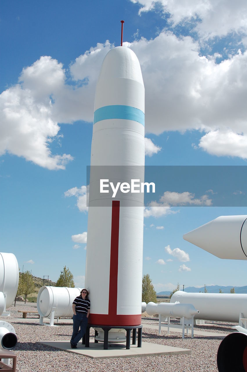 Woman standing by artificial rocket against blue sky