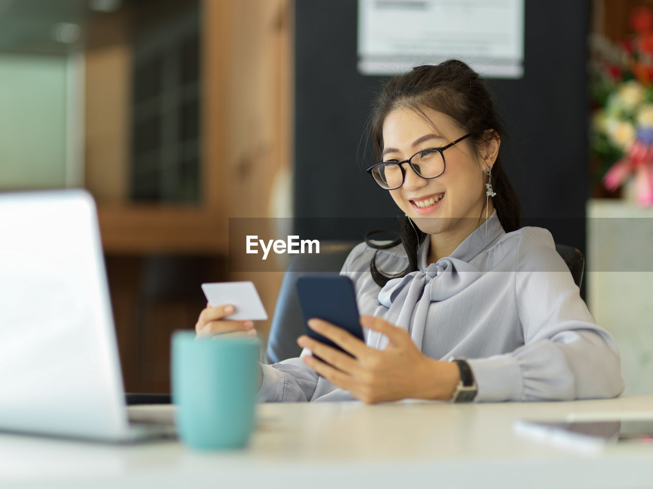 Woman holding visiting card while sitting by laptop on table in office