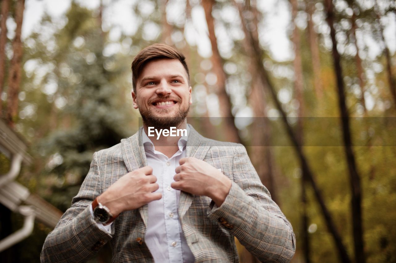 Low angle view of businessman smiling while standing against trees