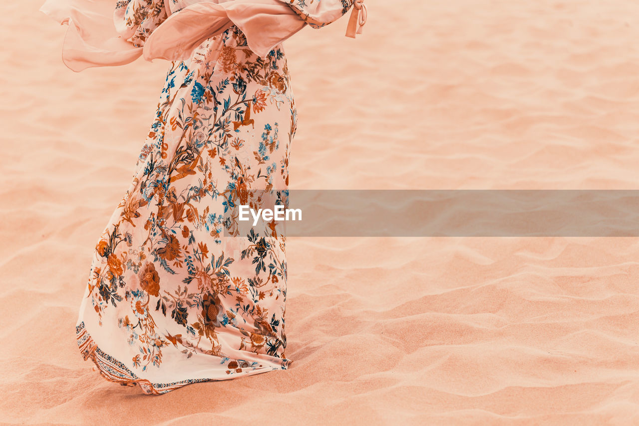 Midsection of woman standing on beach, wind blowing her wide colorful dress