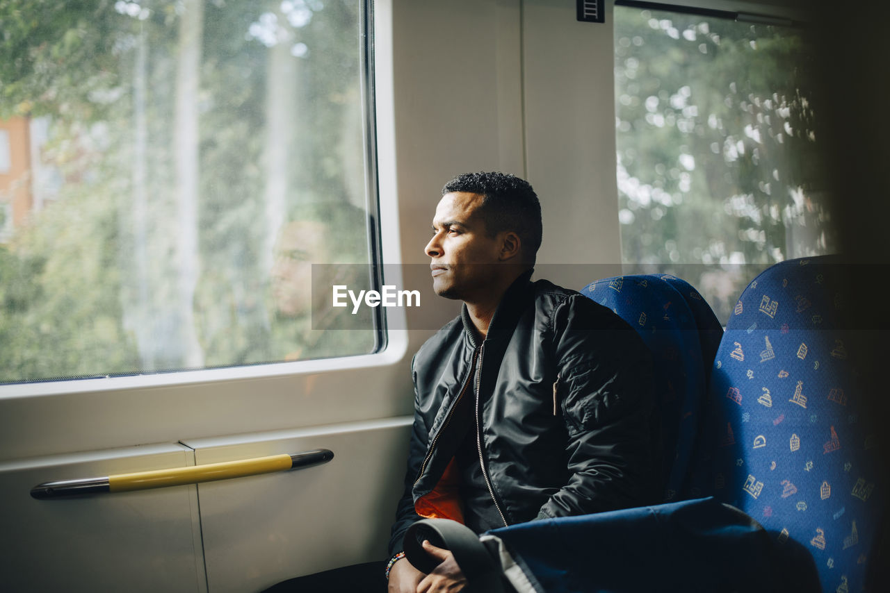 Thoughtful man looking through window while sitting in train