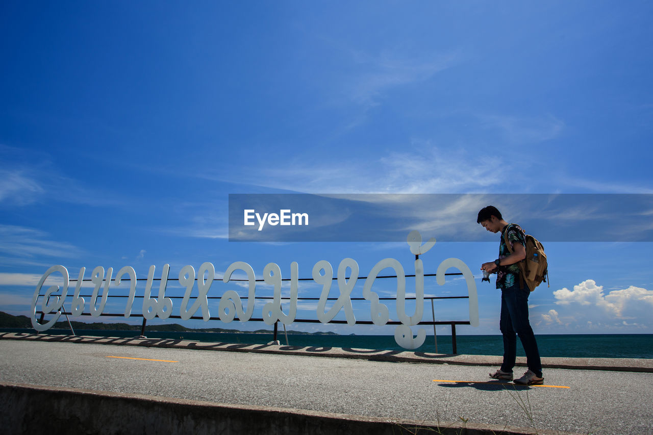 Side view of man standing by text against blue sky