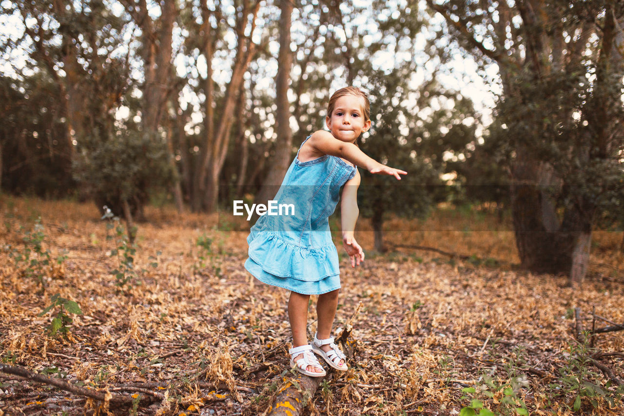 Full length portrait of girl balancing on fallen tree trunk in forest