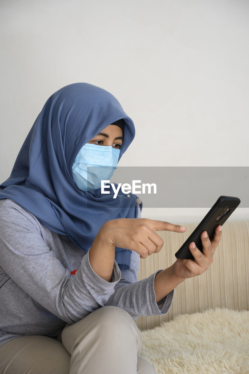 A hijab woman is wearing masker while looking at her smartphone in covid 19 pandemic situation