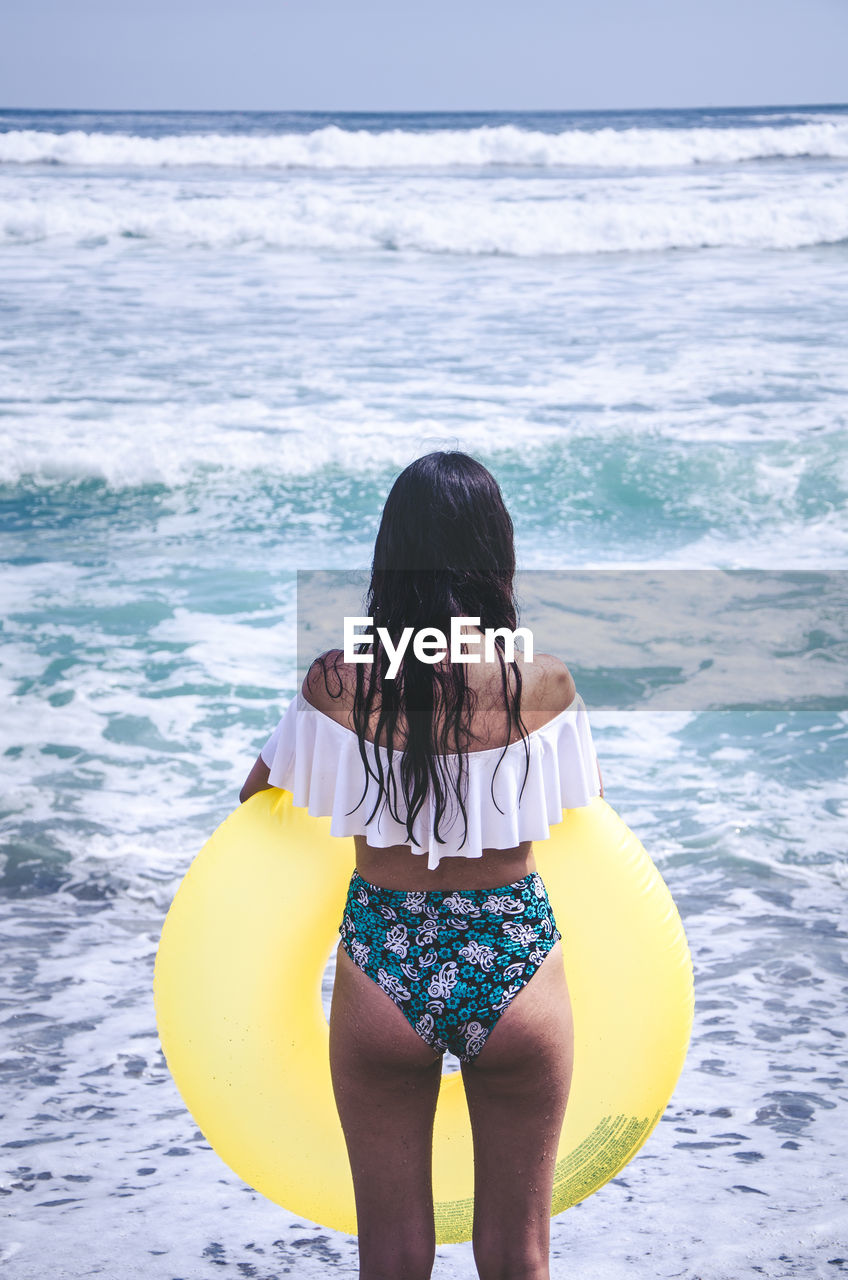 Rear view of woman wearing swimwear holding inflatable ring while standing in sea