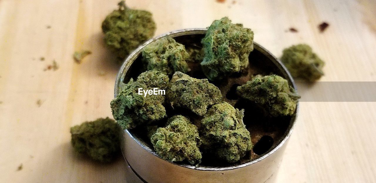 Tight, harvested marijuana nuggets sitting in steel grinder, with two in background 