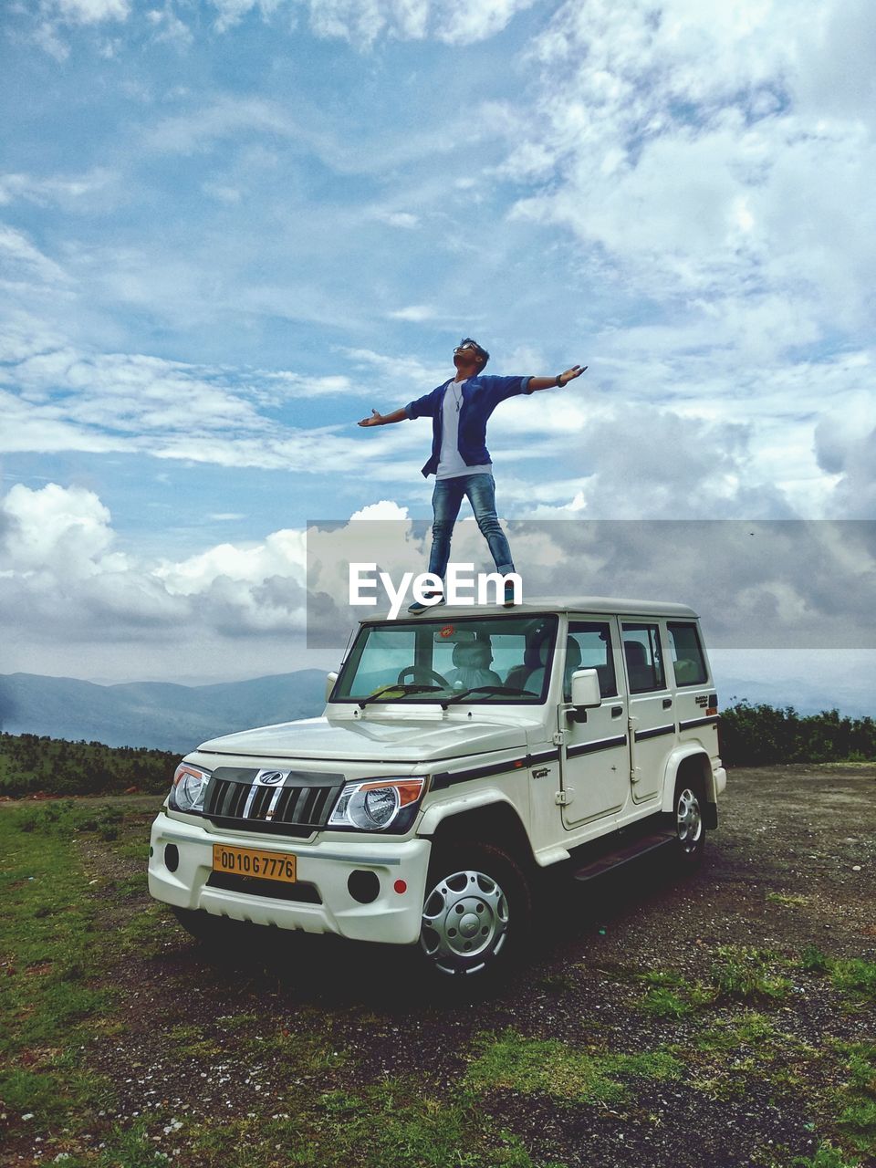 MAN STANDING ON CAR ON FIELD