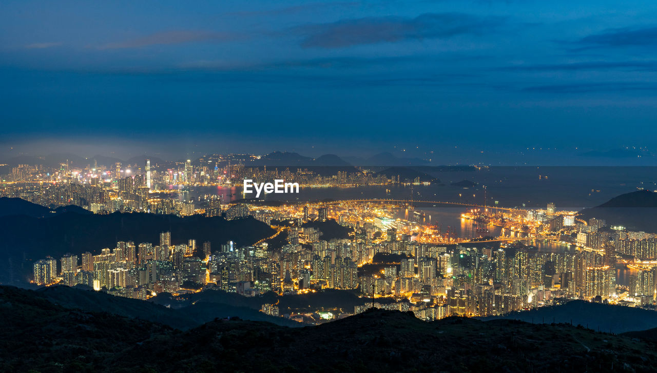 High angle view of illuminated city by sea against sky at night