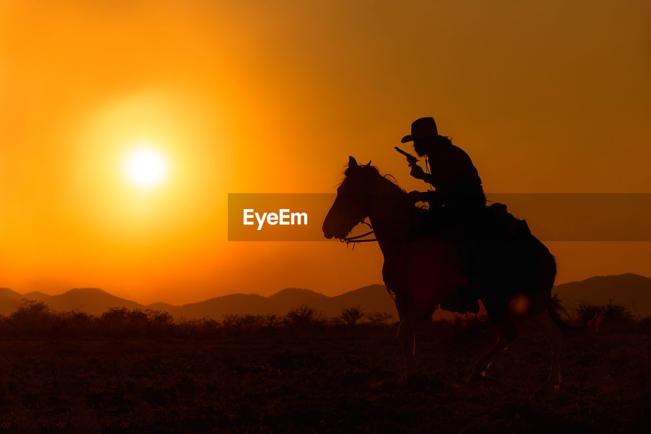 Silhouette riding horse on field against orange sky