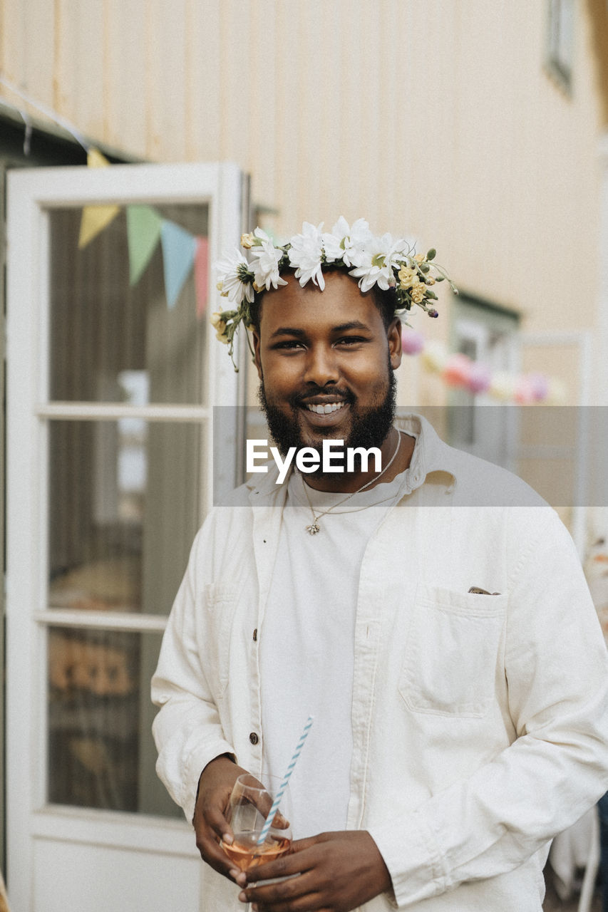 Portrait of smiling young man wearing tiara while holding wineglass during dinner party at cafe