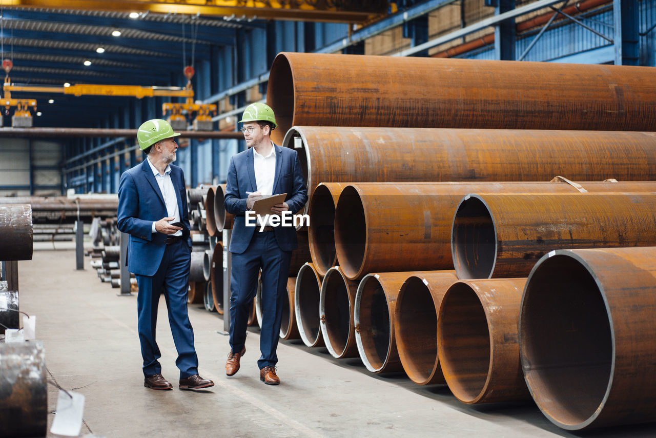 Male managing director discussing with coworker while walking in warehouse