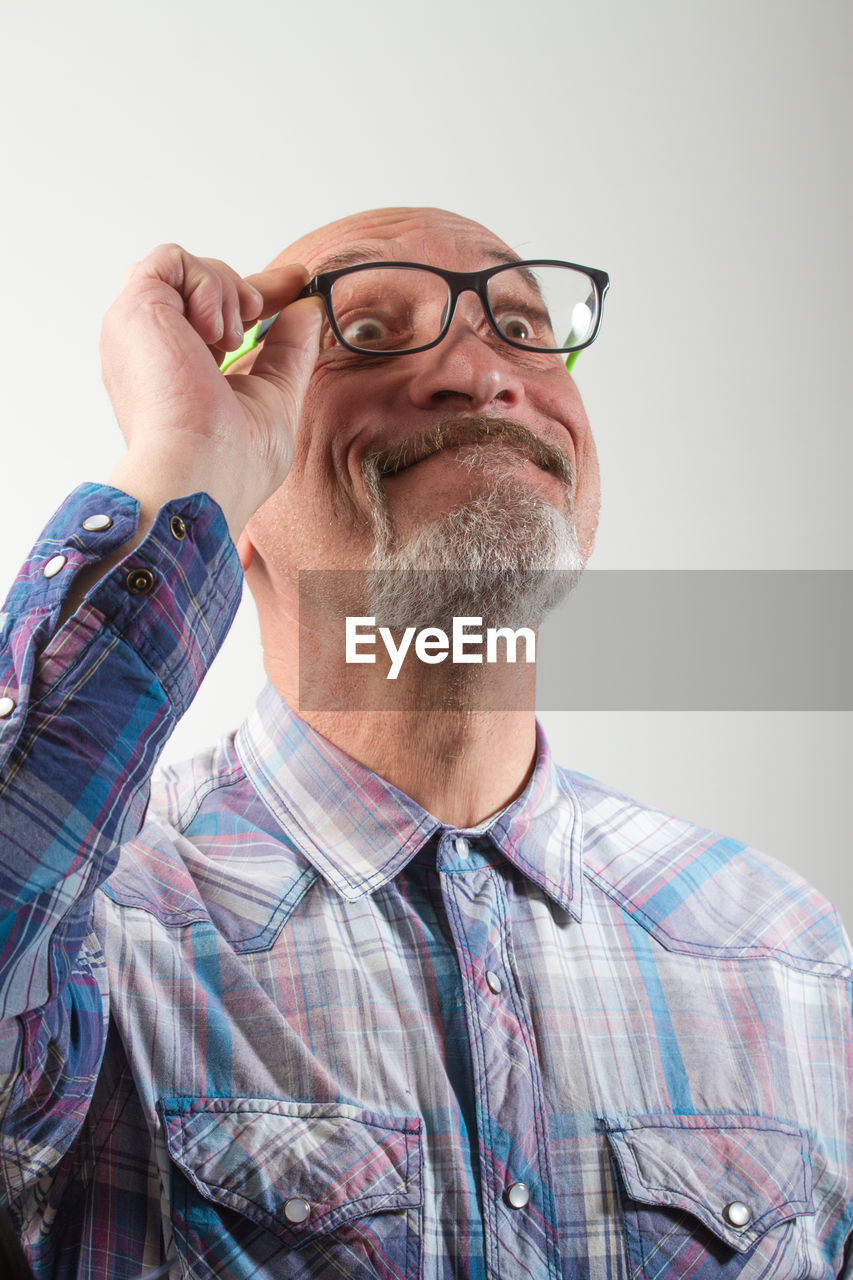 Mature man holding eyeglasses against gray background