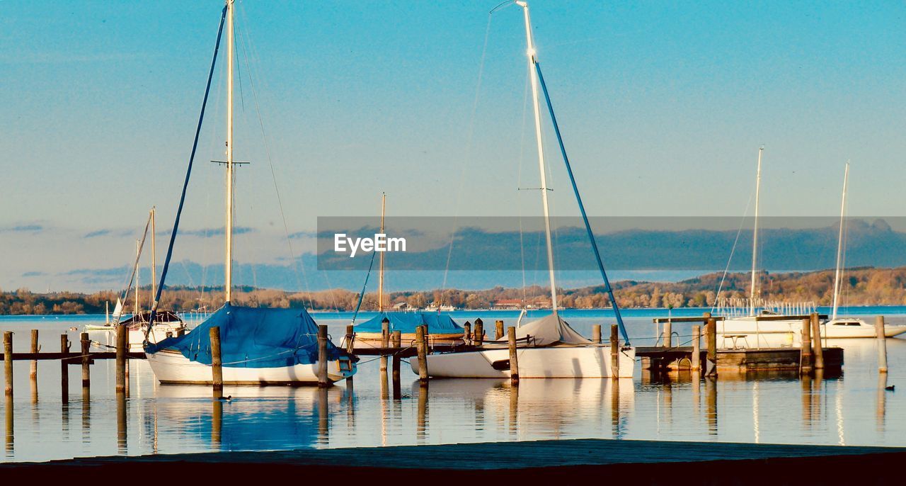 Boats moored at harbor against blue sky