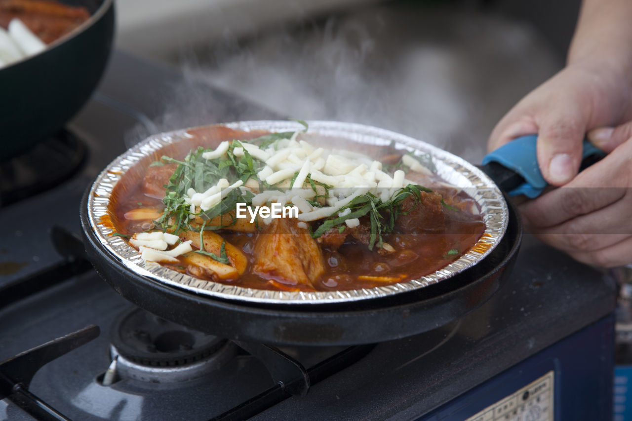Cropped image of woman preparing food in foil container on stove at street