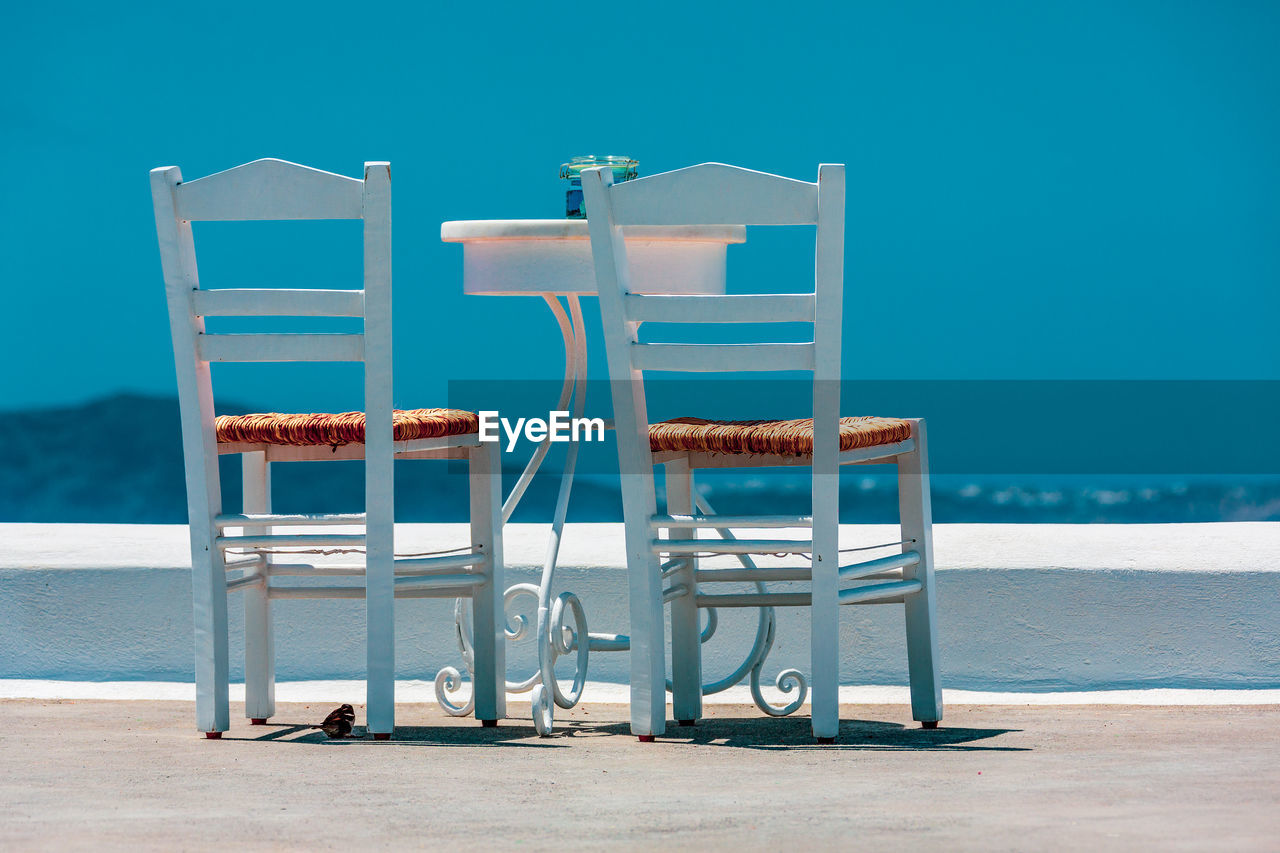 Two chairs and a table on white terrace, santorini greece.