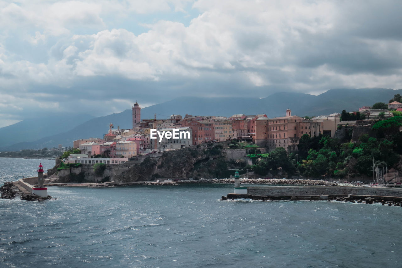 Buildings by sea against cloudy sky