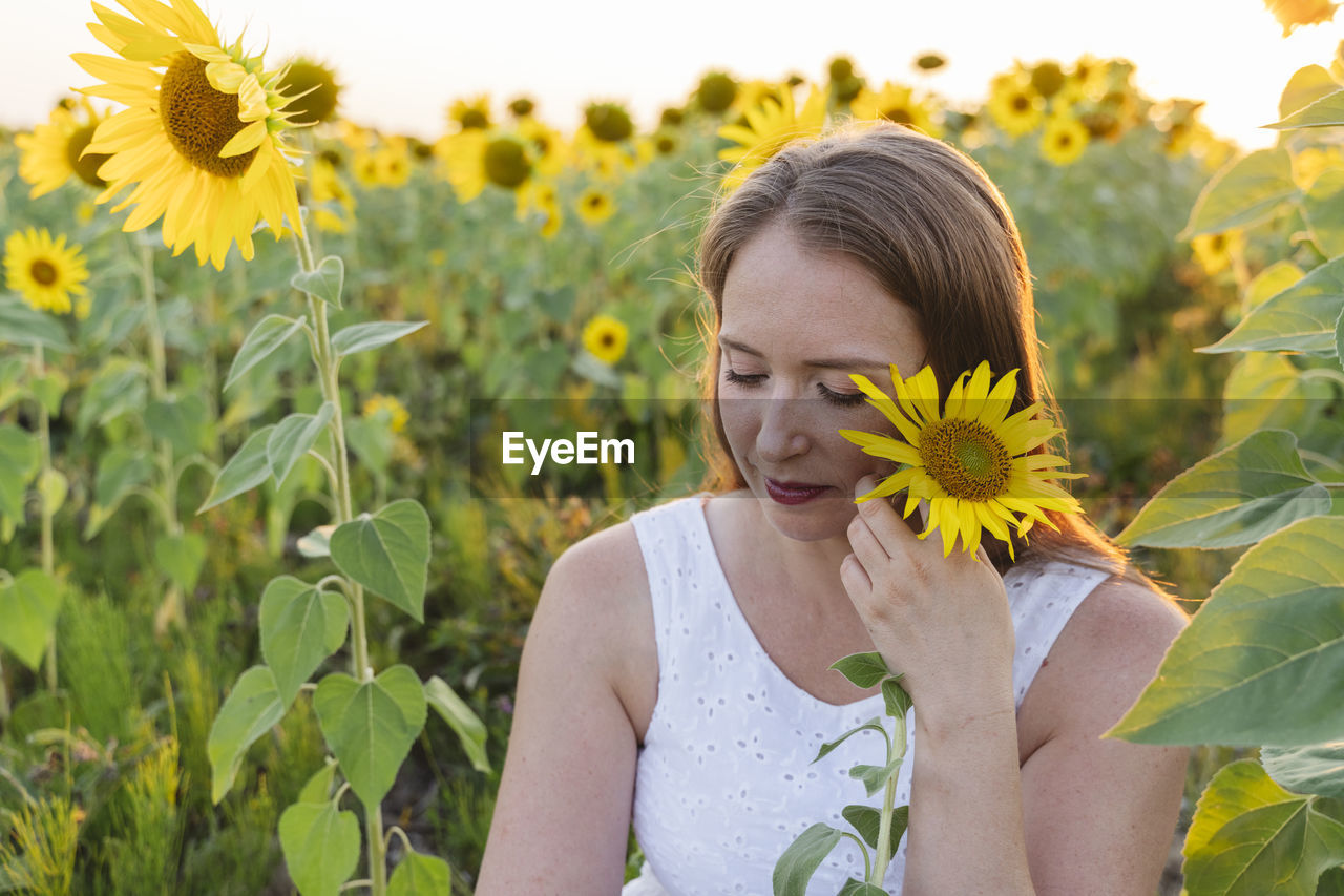 Woman holding sunflower sitting in field