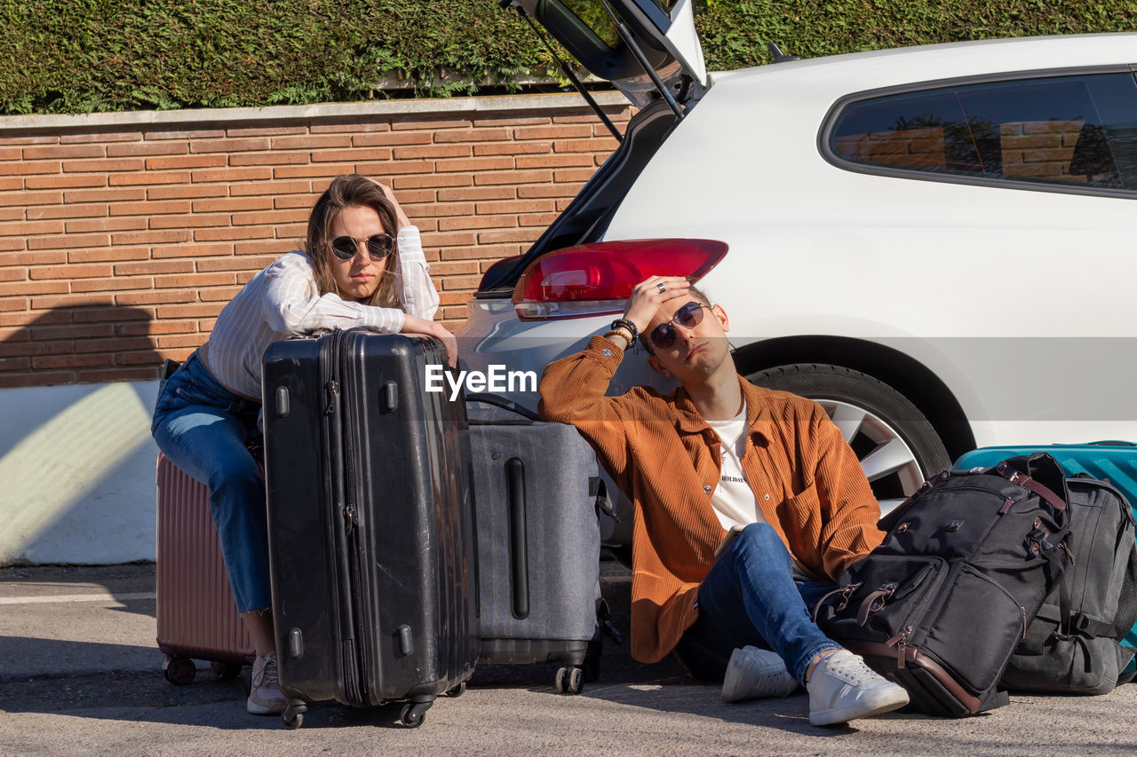 Man and woman sitting on the floor tired and desperate with the luggage in the car trunk